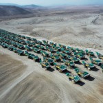 20 lines and 100 number of mining dump trucks located middle of the picture and left and right side is a mountains. the huge truck in middle of them has green lights and cargo and body that resembles like the robots in the Transformers movie