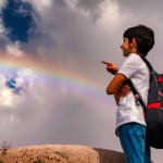 پسربچه ای ایرانی، کوله پشتی بر پشت در حال اشاره به ابرهای آسمان و رنگین کمان