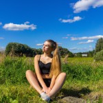 دختری زیبا با موهایی بلوند نشسته روی چمنزار