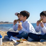 کیم تهیونگ و جئون جونگ کوک جوان با دوتا پسر بچه هایشان در ساحل نزدیک دریا در حال خوردن ساندویچ