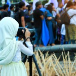 تصویر یک دختر محجبه ی عکاس که در یک جلسه بزرگ در حال عکاسی است