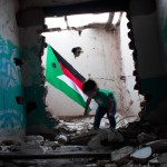 تصویر کودکی فلسطینی که در دست او پرچم فلسطین است و در یک خانه خراب شده در حال بازی کردن است