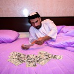 عکس یک شیخ که بر روی تخت خود دراز کشیده و پول هایش را میشمرد