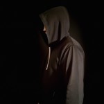 یک پروفایل میخام با بک گراند مشکی از مردی که هودی مشکی پوشیده و رو به دوربین صاف ایستاده و کلاه هودی را روی سرش انداخته و چهرش مشخص نیست