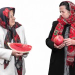 عکس از یک مادر بزرگ با چادر، یک انار در دست مادر بزرگ، مادر بزرگ چادر سفید گل گلی دارد، در کتر او یک دختر سی ساله با شال و مانتو، در دست دختر یک قاچ هندوانه است، بک گراند ایزوله سفید