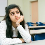 یک دختر نوجوان ایرانی که داره پشت میزش داخل کلاس درس به صورت نگران و ناراحت فکر می کنه