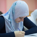 دختر محجبه نگران پشت میز کلاس درسی 
 نشسته و داره امتحان میده