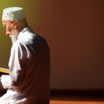 یک روحانی در محراب مسجد، رو به قبله، در حال قرائت قرآن است، چهره کاملا مشخص است