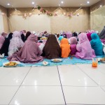 عکس تعداد ۵۰ خانم محجبه چادری با فرزندان خود روی زمین کنار سفره افطار درمسجد نشسته اند