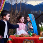 کودکان با لباس های محلی ایرانی با رنگ های مختلف دور سفره هفت سین که در کوهپایه قرار دارن و پشت سرشون کوه دماوند قرار داره