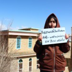 تصویر یک دانش آموز دختر در یک روستا که یک تابلو دستشه و روی تابلو نوشته دبیرستان مستوره اردلان و عاطفه سبس