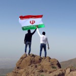بر فراز قله کوه پرچم ایران بر افراشته شده و مردان ایرانی در پایین کوه دست در دست هم داده اند با پرچم ایران