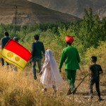 یک عکس از اقوام مختلف ایرانی که لباس محلی پوشیده اند و در دامنه های سرسبز زاگرس در کنار فرزندانشان در حال قدم زدن هستند و پرچم ایران در دست دارند