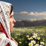 یک بانوی ایرانی در سمت چپ تصویر در حالی که پشت آن به دوربین است و چادر سفید با گلهای رز قرمز که اندازه ی گلها ریز است به سر دارد و زن در دشتی پر از گلهای بابونه قرار گرفته که از دور اسمان ابی و کوهها پیدا هستند